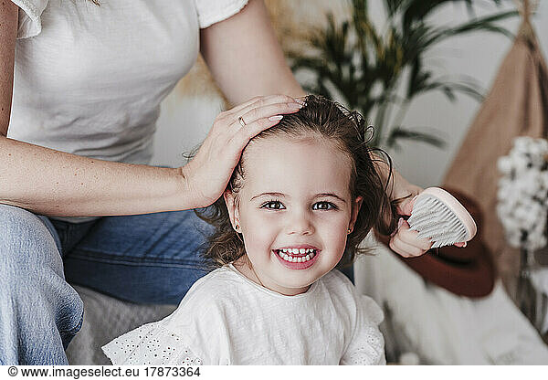 Mother brushing cute daughter's hair at home