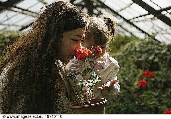 Mother carrying daughter and smelling red flowers in greenhouse