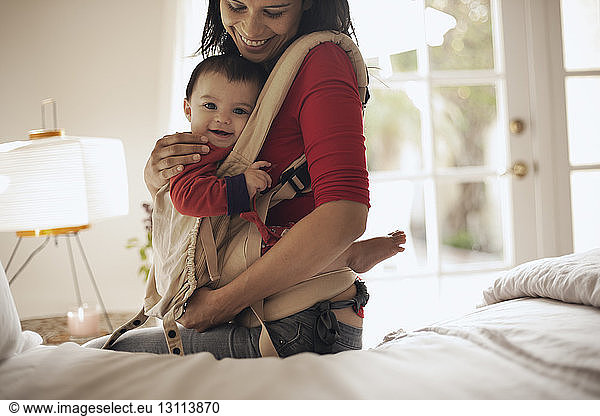 Mother carrying daughter while sitting on bed at home