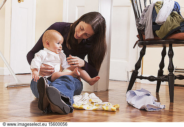 Mother changing her son's clothes while sitting on the floor