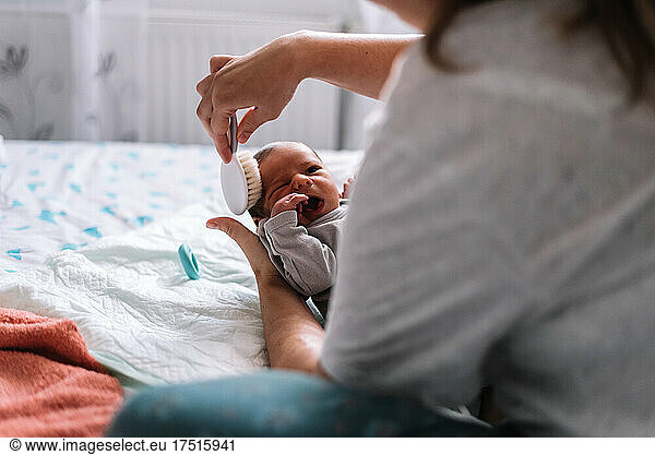 Mother combing her baby's hair in bed.
