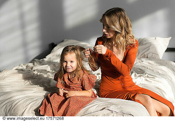 Mother combing her daughter's hair in bed