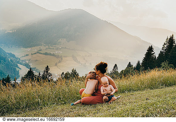 Mother cuddling with her boys sitting on the grass in the Alps