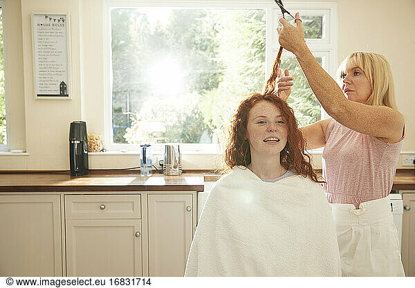 Mother cutting hair for preteen daughter in sunny kitchen