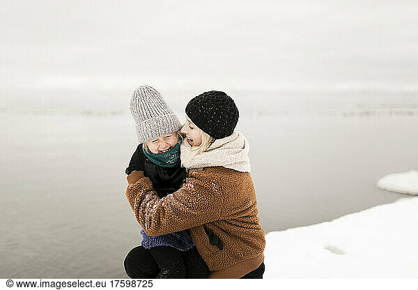 Mother embracing daughter by lake in winter