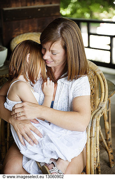 Mother embracing daughter while sitting on chair
