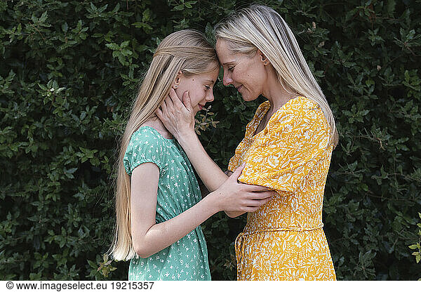 Mother embracing daughter with eyes closed in front of plants