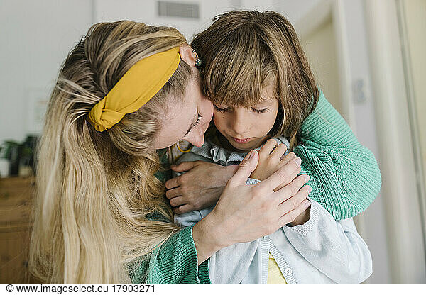 Mother embracing depressed daughter from behind at home