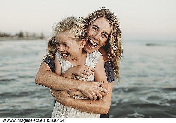 Mother embracing young girl with freckles in ocean laughing