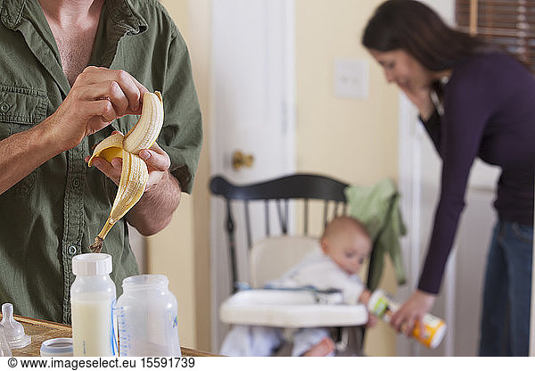 Mother feeding her son while father peeling a banana