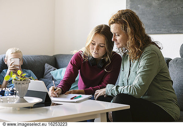 Mother helping daughter study while son using phone at home