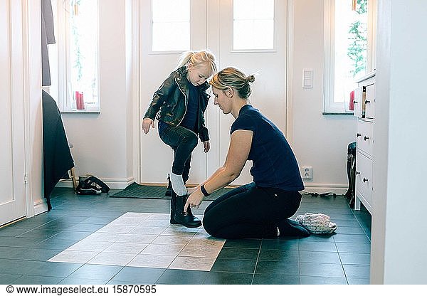 Mother helping daughter with shoes near door at home