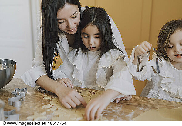 Mother helping daughters in making cookies for Easter