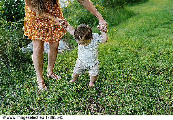 mother helping her baby learn to walk in the grass outside