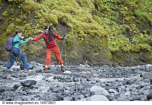 Mother helping her daughter jumping over river in Iceland