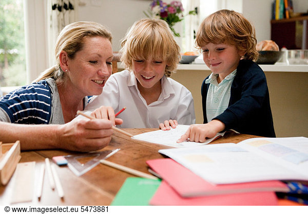 Mother helping older son with homework at the kitchen table