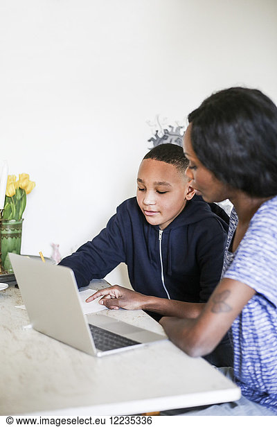 Mother helping son in doing homework with laptop on table at home