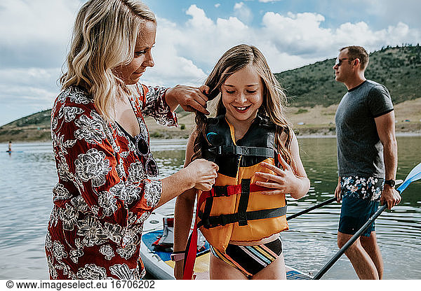 Mother helps happy daughter tighten life vest on a sunny day