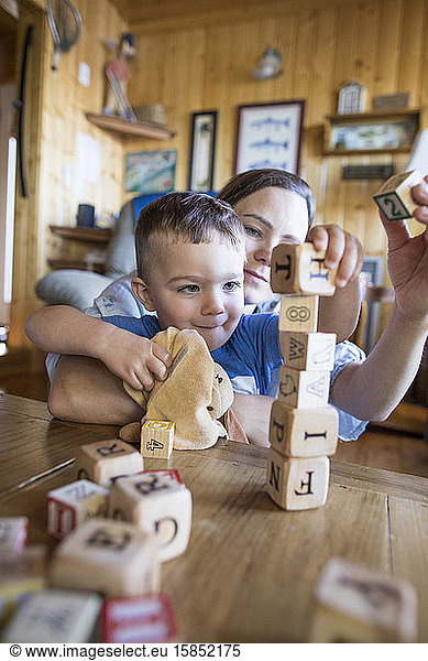 Mother helps her son build a tall tower out of wooden blocks.