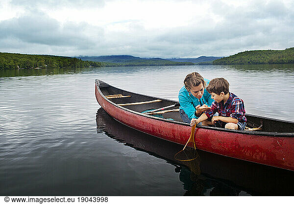 Mother helps young son look for fish over side of canoe at Kezar Lake