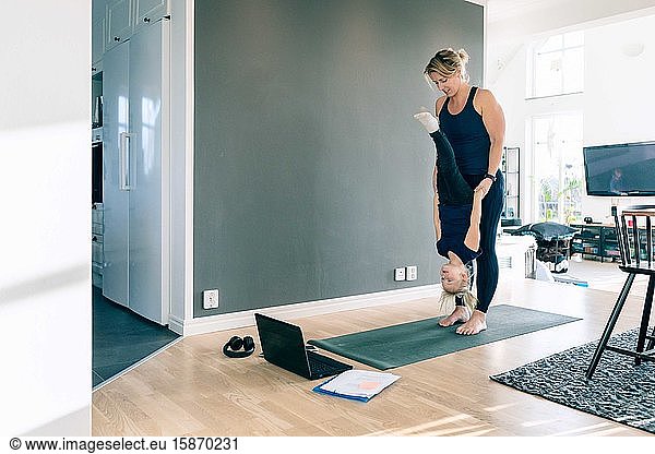 Mother holding daughter upside down while standing on mat in living room