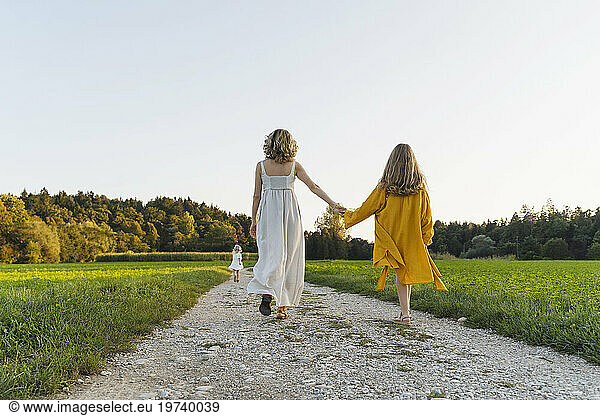 Mother holding hands with daughter and walking on dirt road