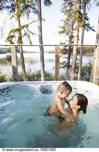 Mother holds her son in hot tub at the lake.
