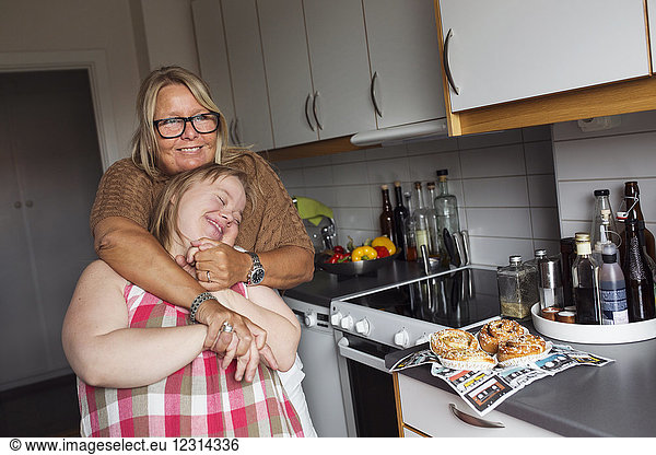 Mother hugging daughter with down syndrome in kitchen