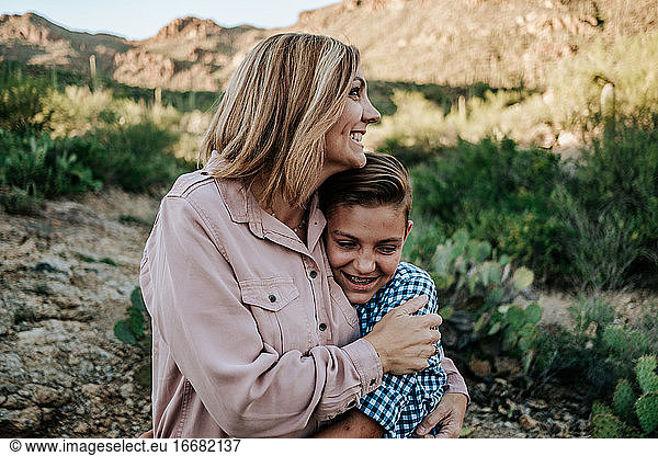 mother hugging smiling non binary child in the desert