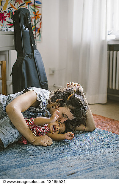 Mother kissing daughter lying on carpet at home