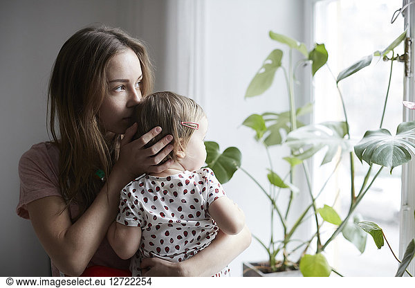 Mother kissing daughter while looking through window at home