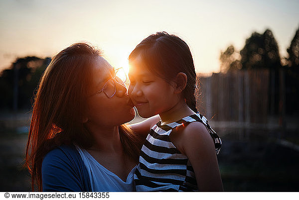 Mother kissing her daughter during sunset