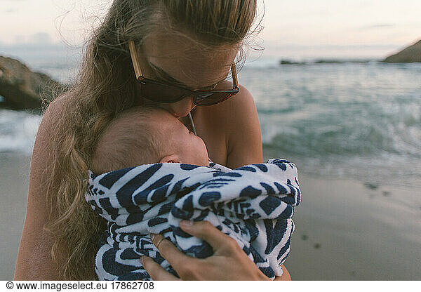 Mother kissing sleeping baby on beach in the evening