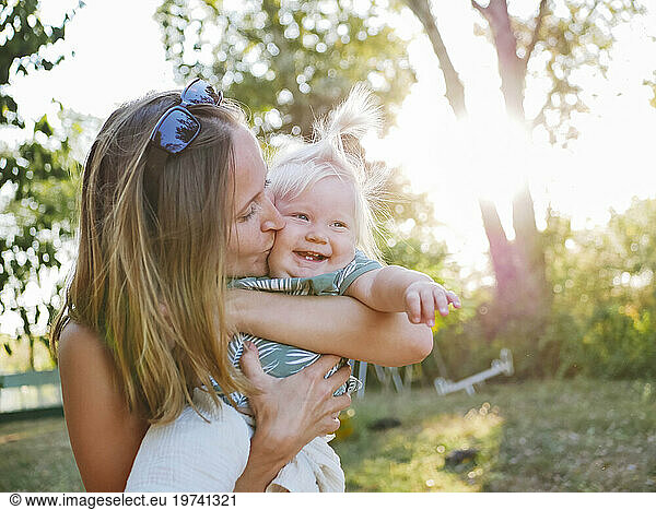 Mother kissing smiling daughter at park