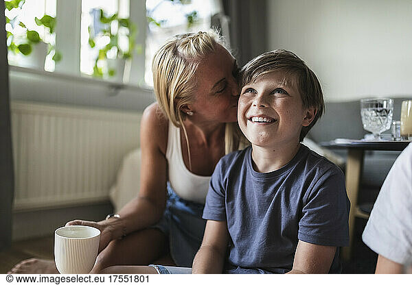 Mother kissing smiling son watching TV in living room
