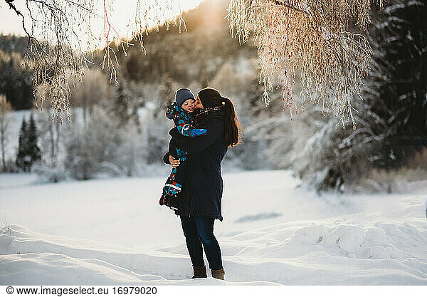 Mother kissing son in mountains full of snow on sunny winter day