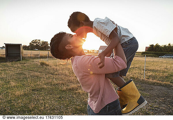 Mother kissing son while carrying him at farm during sunset