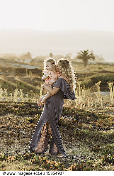 Mother kissing toddler daughter at beach during sunset