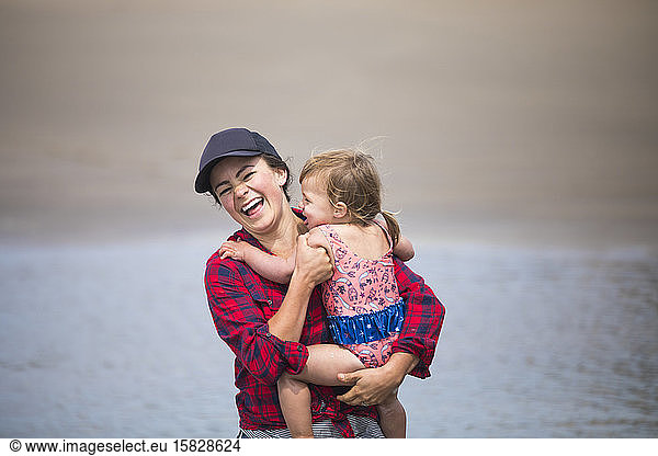 Mother laughing while holding baby girl at the beach.