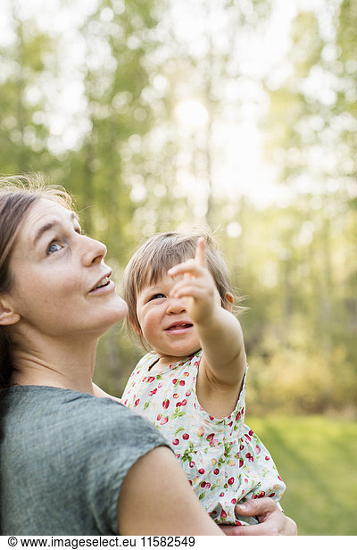 Mother looking at baby girl pointing upwards in forest