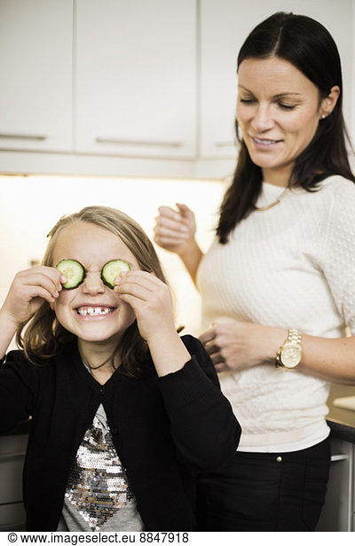 Mother looking at daughter covering eyes with cucumber slices