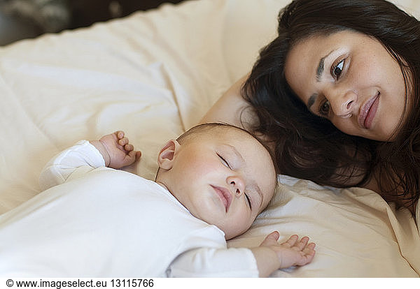 Mother looking at daughter sleeping on bed at home