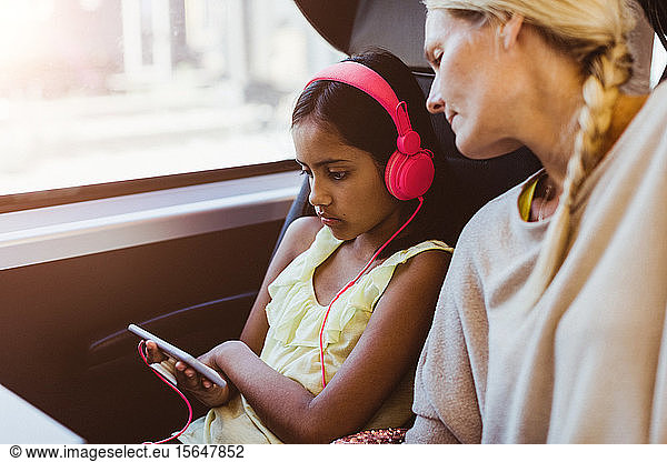 Mother looking at daughter watching movie on smart phone while traveling in train