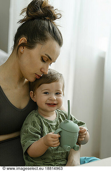 Mother looking at smiling daughter holding sipper bottle at home