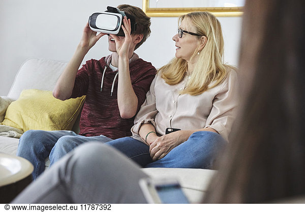 Mother looking at son using virtual reality headset while sitting on sofa