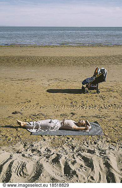 Mother lying on sand with son in stroller at beach
