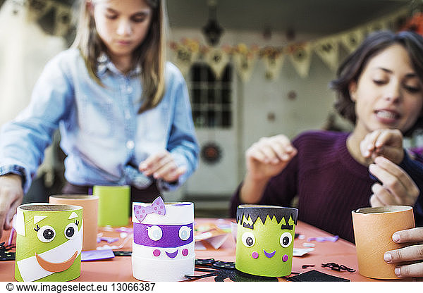 Mother making various decoration with children at table during Halloween party