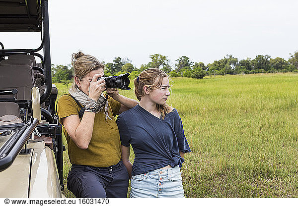 mother photographing with teen daughter near safari vehicle  Botswana