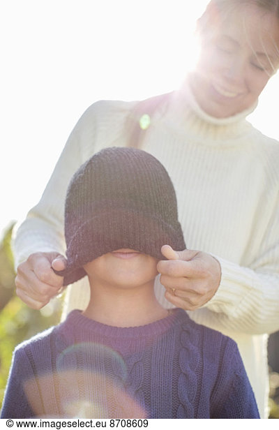 Mother putting knit hat to son at yard
