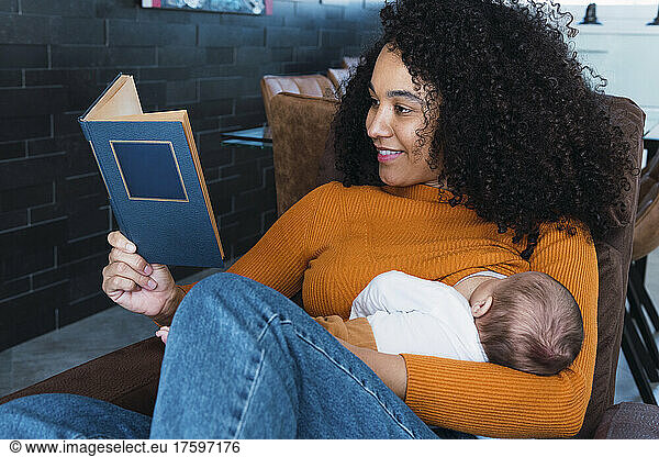 Mother reading book and breastfeeding son at home